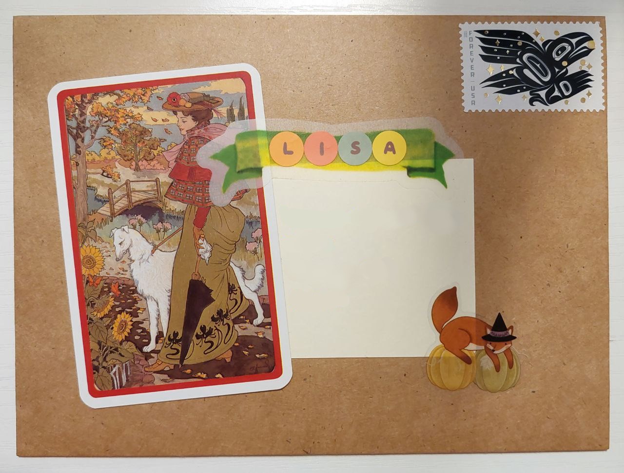 a photo of a brown envelope with an illustration of a woman with her white dog. it has a fall setting and a wind is blowing leaves in the background. there is a green banner with round stickers that spell out 'lisa' in autumn-themed colors. there is also a sticker of a fox on a pumpkin in the lower right corner