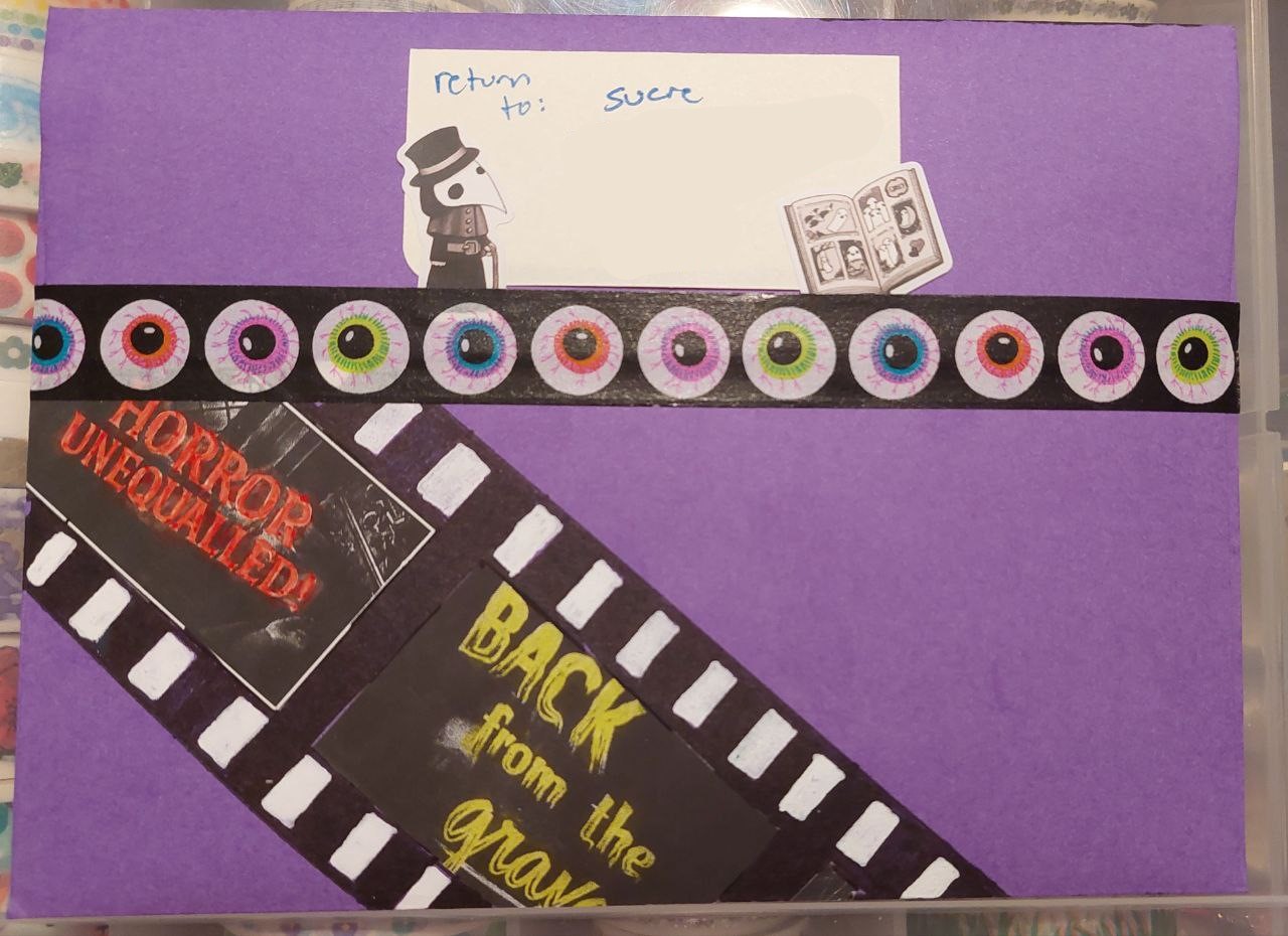 photo of the back of a purple envelope. a handmade film strip runs diagonal across the back. it has old horror movie title cards on them. there is a return label that reads 'sucre' and has cute ghost stickers in the corners. eyeball washi tape seals the envelope shut
