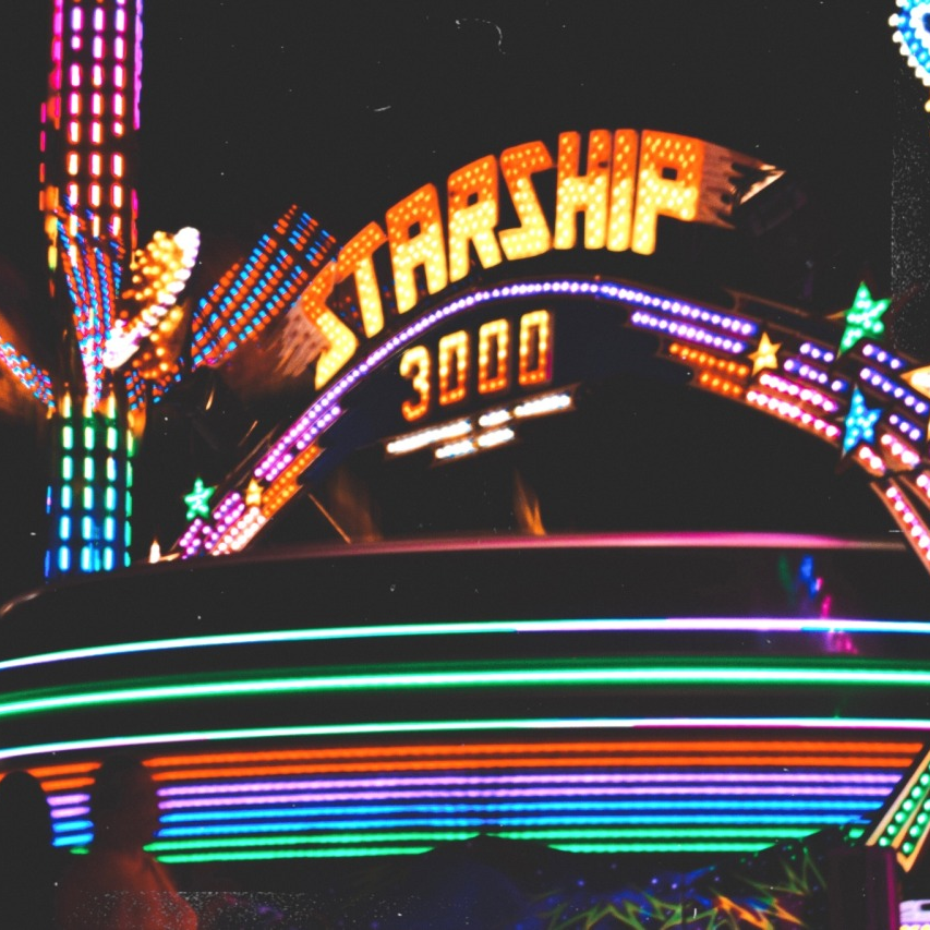 photo of a carnival ride at night. the ride has a sign that reads STARSHIP 3000 on top and is lit up in bright lights.
